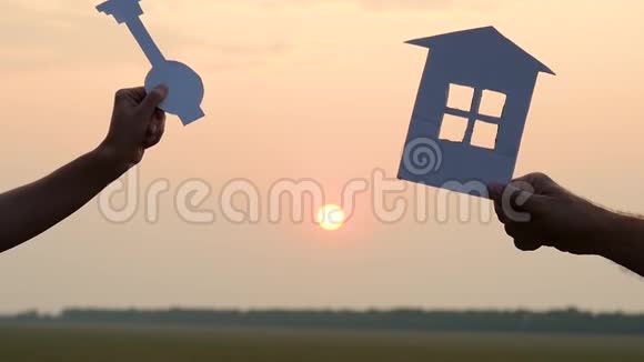 双手特写手持纸房和夕阳背景上的一把钥匙视频的预览图