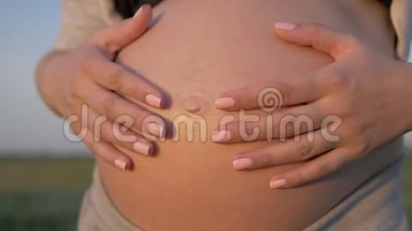 在夕阳下孕妇用手在胃上形成一颗心视频的预览图