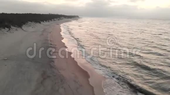 日落后蓝色小时的波罗的海海岸鸟瞰图暮光的海岸线带着滚滚的波浪空旷的海滩视频的预览图