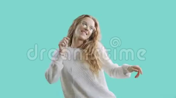 戴着耳机的快乐年轻女子正在用智能手机听音乐在蓝屏背景下跳舞和微笑视频的预览图