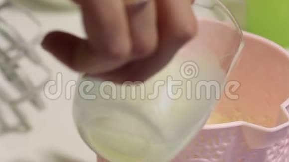 一个女人把牛奶加入容器然后和搅拌机混合为突触准备糖霜视频的预览图