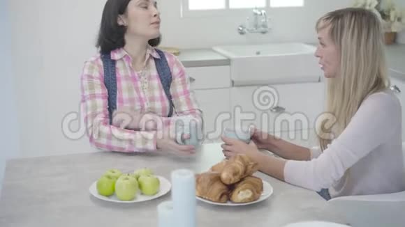 金发成年白种人女人坐在桌边和她的黑发朋友说话两个女人在一起一天视频的预览图
