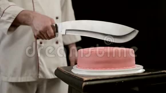 穿着厨师制服的人在黑色背景上拿着刀在蛋糕上切特写视频的预览图