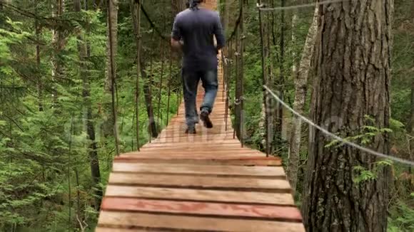 绿色森林中男性游客穿越木质悬索桥后景库存录像一个走着的男人视频的预览图