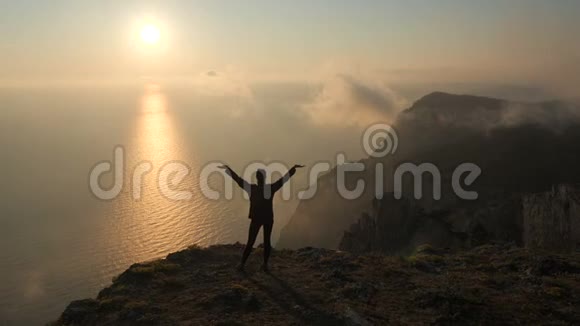 年轻女子席勒瓦特举起双臂伸出手从高高的海面上看着美丽的戏剧性日落视频的预览图