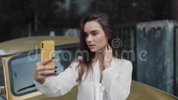 年轻女子在智能手机上自拍白天站在户外的女孩微笑着吹吻视频的预览图