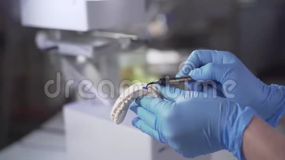 高加索手在防护手套上的特写在铸造的牙齿上涂上蓝色的油漆牙科技师改建视频的预览图