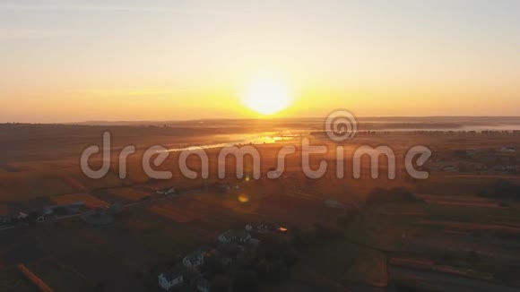 在日落时分在有房子的田野上快速跟踪无人机的镜头速度减慢接近太阳视频的预览图