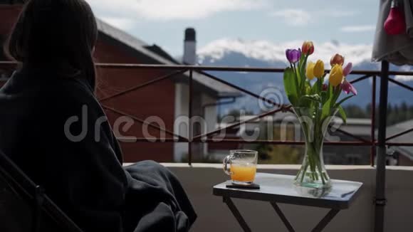 年轻女子在阳台上喝果汁在背景上喝雪山假期和放松美丽的女孩欣赏风景视频的预览图
