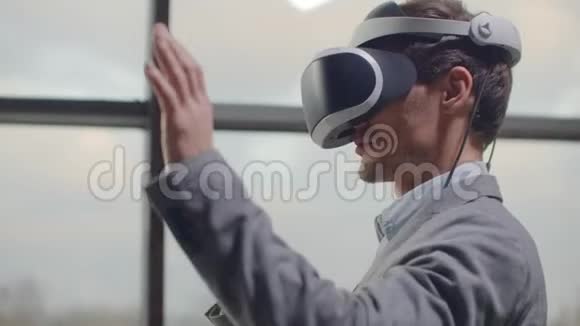 男人戴着虚拟现实的头盔背景是工作场所办公室的一扇巨大的窗户设计视频的预览图