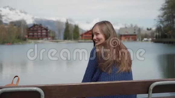 美丽的长发女人坐在湖边的木凳上有着美丽的山景然后女孩回头看视频的预览图