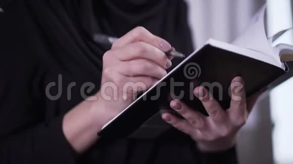 特写女性手写书在家中穿着传统服装和戴头巾写作的无法辨认的穆斯林妇女视频的预览图