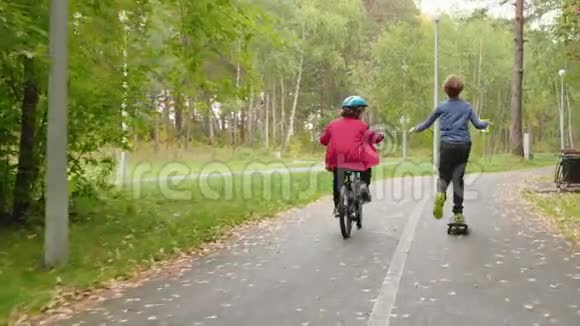 秋季公园青少年男孩骑自行车和滑板的后景视频的预览图