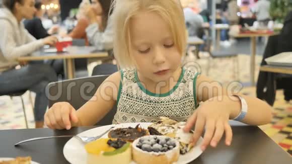 小女孩在一家背景模糊的咖啡馆里尝试各种蛋糕视频的预览图