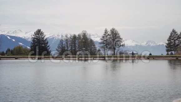 女孩从风景如画的湖岸的长凳上站起来离开了松树和山脉是背景视频的预览图