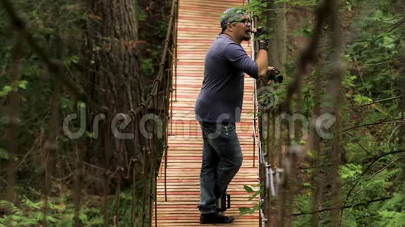 站在木制吊桥上休息的人的侧视库存录像男人看着视频的预览图