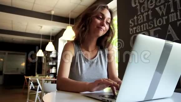 慢动作年轻微笑的女人在咖啡馆用笔记本电脑打视频电话视频的预览图