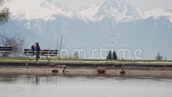 年轻女子坐在木凳上通过智能手机拍照可以看到令人惊叹的山湖景色视频的预览图