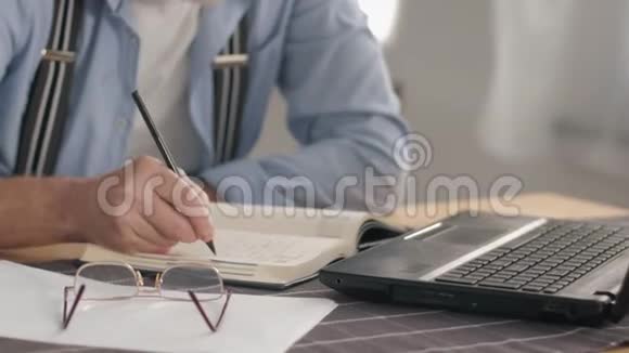 现代退休自由职业者的画像他在家里的便携式电脑上工作并在笔记本上写账单微笑着视频的预览图