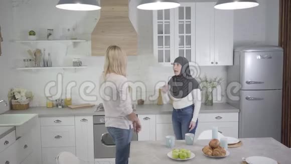 成年白种人和穆斯林妇女在家里争吵戴头巾的女士回头找朋友两个朋友在室内争吵视频的预览图