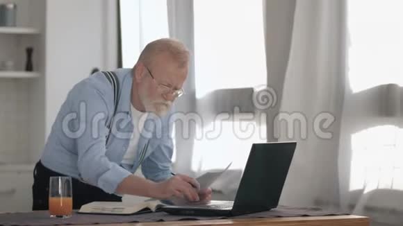 在家的笔记本电脑里工作时有着灰色胡子和视力眼镜的老年男性感到很担心视频的预览图