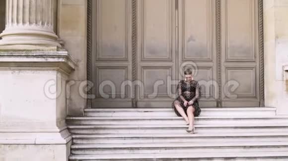 迷人的性感女人坐在历史建筑的楼梯上在镜头前摆姿势行动金发女郎视频的预览图