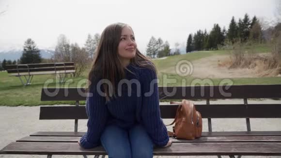 微笑的年轻女子坐在木凳上在阳光明媚的春日可以欣赏到湖光山色的美景视频的预览图