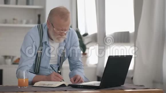 戴眼镜长胡子戴眼镜的老人在家里的笔记本电脑上自由工作这种生活方式活跃了现代社会视频的预览图