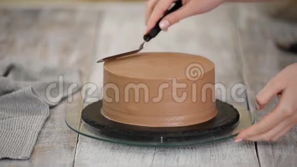 年轻的女人正在装饰巧克力蛋糕站在家里的厨房里女人完成糖霜巧克力蛋糕视频的预览图