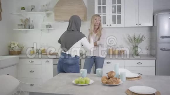 成年金发白种人女人与穆斯林女性朋友争吵的肖像两个女人在现代厨房争吵视频的预览图