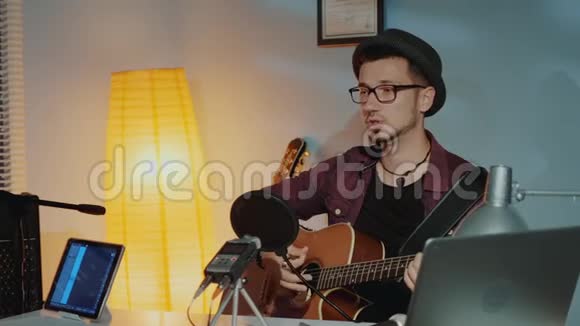 快乐的年轻音乐家在家里的录音室里弹吉他对着麦克风唱歌视频的预览图