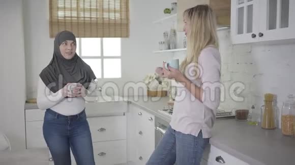 成年穆斯林妇女倾听金发白种人朋友并捧着咖啡杯的肖像多民族视频的预览图
