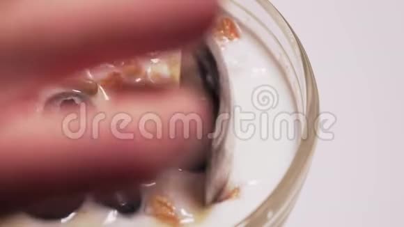 一个女人把酸奶麦片蜂蜜和浆果中的成分混合在一起白色背景下的健康甜点孤立的宏观视频的预览图