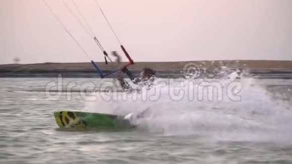 风筝冲浪者在水面上滑行在日落时在他身后的海滩上飞溅视频的预览图