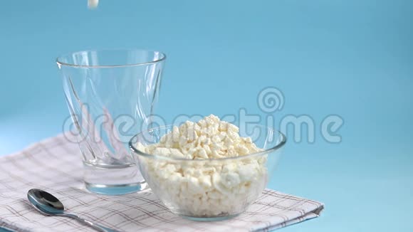 新鲜的干酪放在一个透明的碗里汤匙和一杯蓝色背景的kefir发酵食品视频的预览图