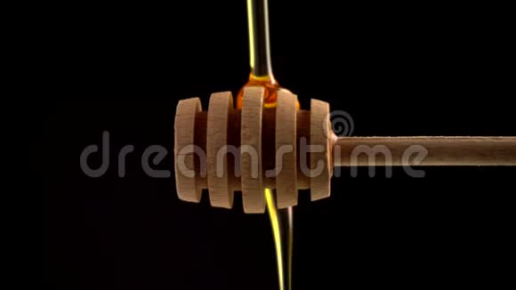 在黑色背景特写镜头上用木勺盛蜜倒入新鲜液体黄色蜂蜜视频的预览图