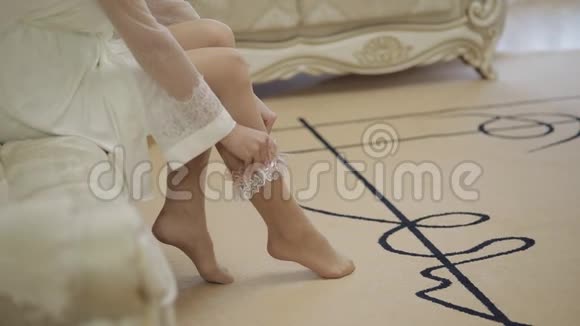 穿着睡衣和面纱的新娘的腿坐在沙发上把吊袜带放在腿上视频的预览图
