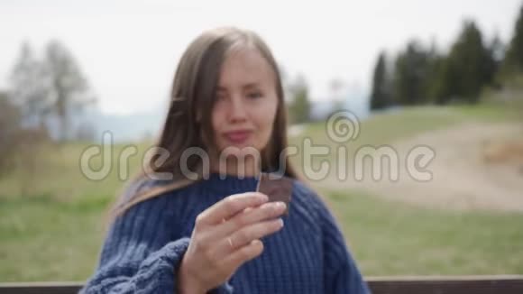 穿着蓝色毛衣的漂亮女孩手里拿着一块巧克力在山里的户外品尝有机会视频的预览图