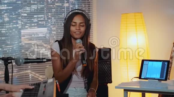 一位美丽的黑人妇女在家庭录音室的乐队排练中有感情地演唱歌曲视频的预览图