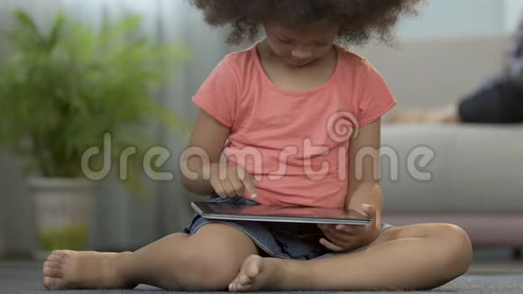 小女孩在平板电脑上玩游戏坐在家里的地板上学前教育视频的预览图