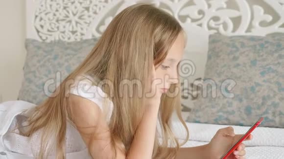 可爱的少女躺在床上用红色手机视频的预览图