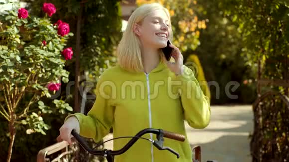带着电话摆姿势的快乐女孩金发女人穿着绿色衬衫兴高采烈手里拿着手机视频的预览图