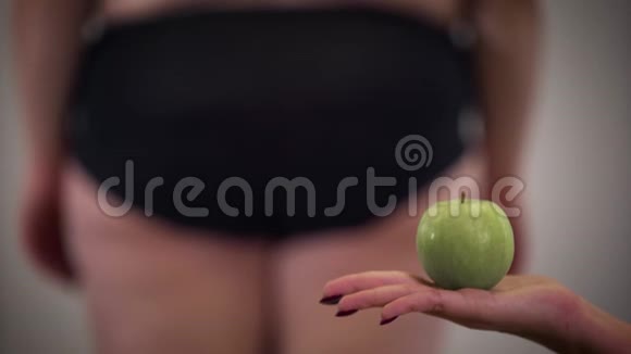 女性白种人手拿苹果的特写镜头是肥胖女性背景是脂肪团健康食品视频的预览图