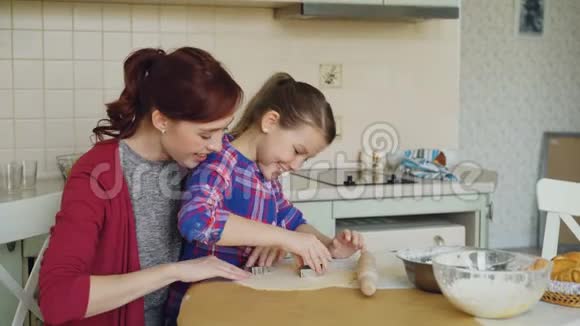 微笑的母亲和可爱的女儿一起做圣诞饼干坐在家里的厨房桌子上家庭食物和视频的预览图