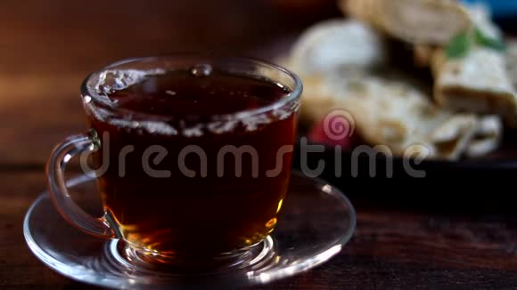 早餐有煎饼和茶把热茶倒进一个透明的杯子里在木制背景上视频的预览图