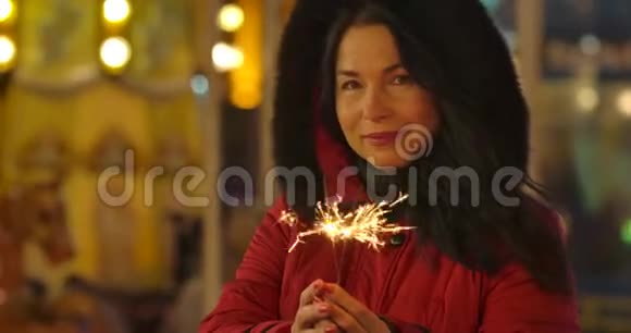 积极的白人妇女的肖像穿着红色外套手持火花和微笑快乐的成年女士享受城市市场视频的预览图