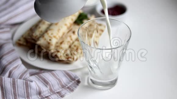 早餐包括煎饼和牛奶牛奶倒入透明玻璃中背景是一个盘子和一张新鲜的餐巾纸视频的预览图