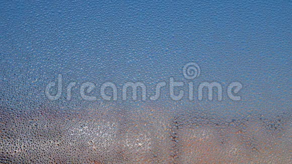 带有水凝结的窗户的扭曲玻璃水滴掉下来了模糊的建筑和蓝天的背景视频的预览图
