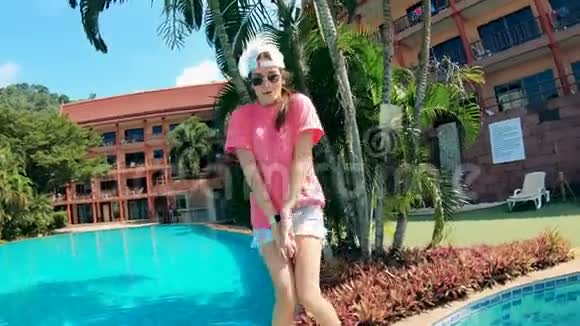 年轻女子正在游泳池和酒店附近快乐地跳舞视频的预览图