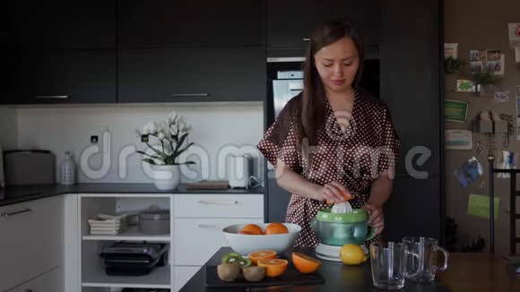 早上在厨房用榨汁机准备橙汁的漂亮女孩穿着棕色晨衣总计划视频的预览图